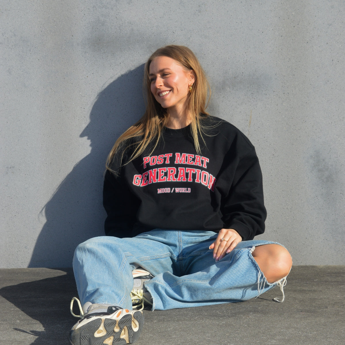 'POST MEAT GENERATION University' Organic Oversize Sweatshirt in der Farbe Black als Frontaufnahme getragen von einem weiblichen Model sitzend